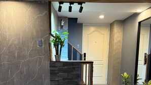 A modern living room with a stone accent wall, a staircase, and a glass coffee table with remote controls and glasses. - Califnia Gardens Square (Mandaluyong)