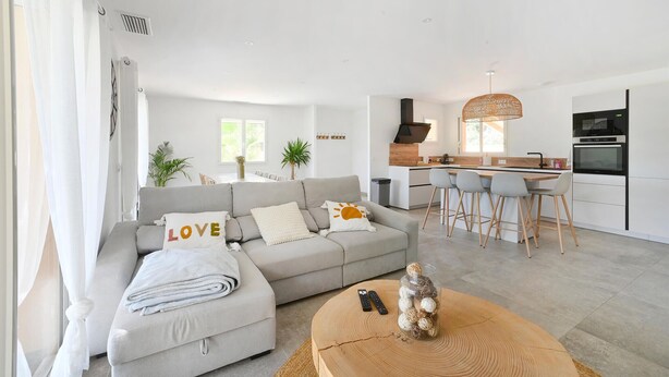 Una sala moderna con un sofá gris, una mesa de centro y una zona de cocina con un juego de comedor.