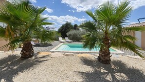 Zona de piscina con dos palmeras, piscina y área de descanso con sombrillas.