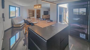 A modern kitchen with a central island, a dining area with a sofa, and a large window providing a view.