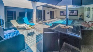 A modern outdoor pool area with lounge chairs, a glass-enclosed space, and a small table with a bowl.