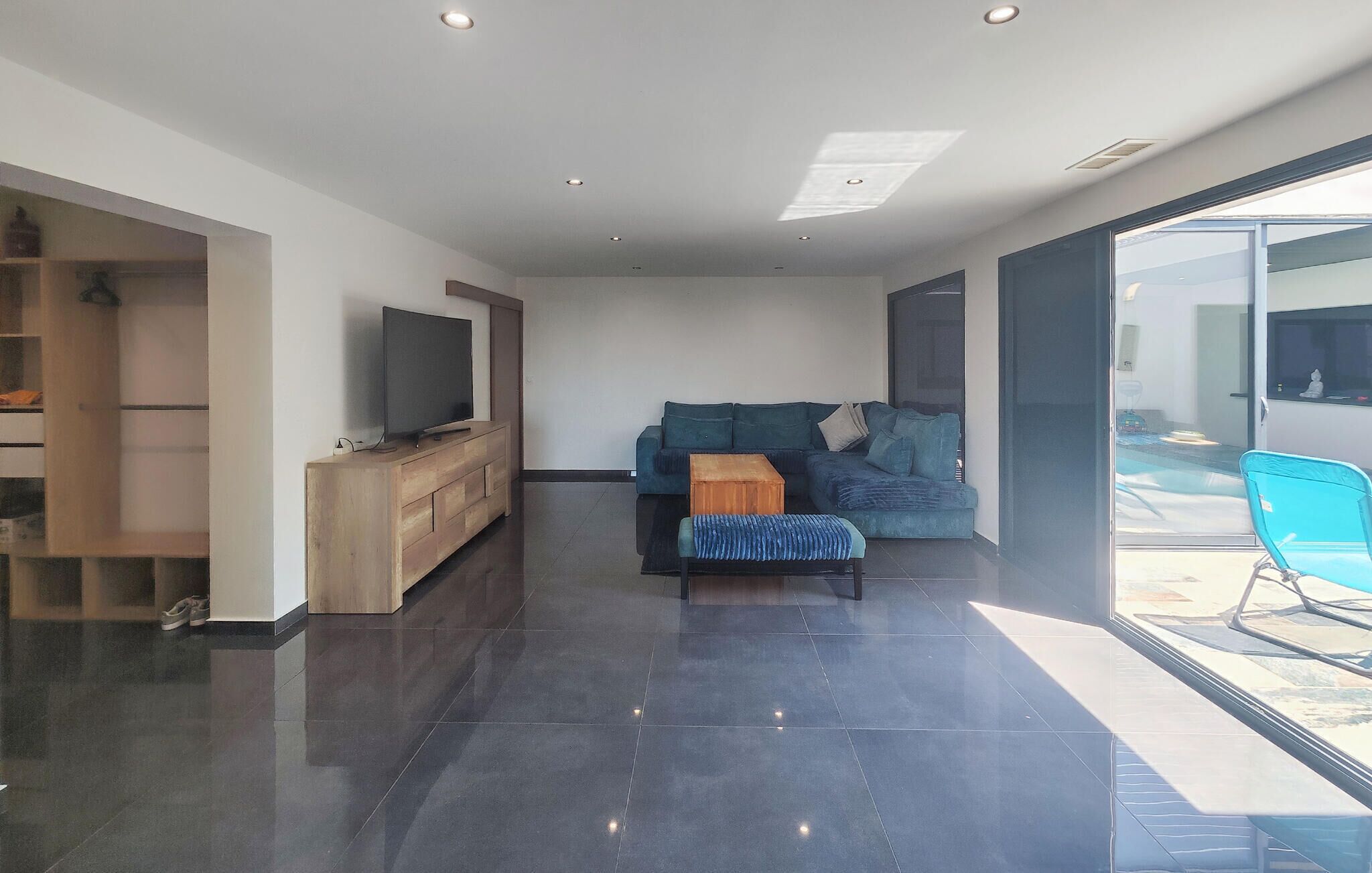 Una sala de estar moderna con un televisor de pantalla plana sobre una consola de madera, un sofá azul con cojines, un pequeño cofre de madera y una silla azul.