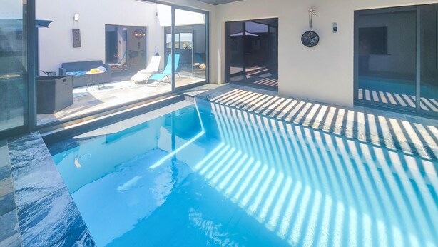 An indoor swimming pool with clear glass walls, a modern design, and a view of the outside patio area.