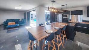 A modern kitchen with a wooden dining table, bar stools, and built-in appliances.