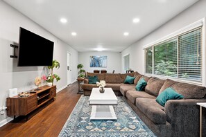 Een moderne woonkamer met een flatscreen televisie, een hoekbank, een salontafel en een kamerkleed met patroon.