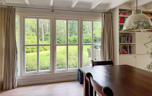 Una habitación con ventanas amplias, una mesa de madera, una estantería y una lámpara colgante.