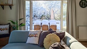 En hyggelig stue med en sofa pyntet med farverige puder, et vindue med udsigt til sneklædte træer, og et vægur.