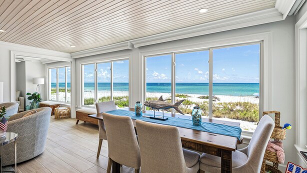 A spacious dining area with a view of the beach, wooden ceiling, and beach-themed decor.