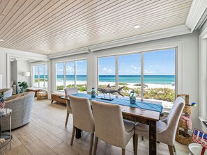 A spacious dining area with a view of the beach, wooden ceiling, and beach-themed decor.