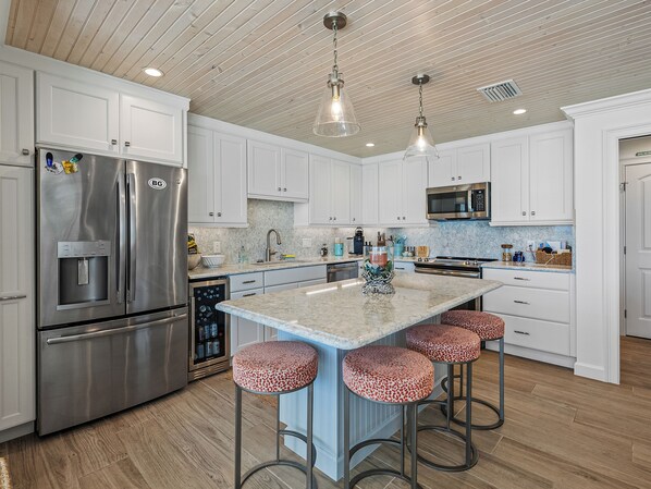 A modern kitchen with stainless steel appliances, a marble countertop, and a central island with bar stools.
