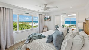 A bedroom with a large bed, a ceiling fan, and a view of the beach.