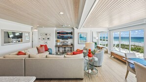 A spacious living room with a large sectional sofa, a coffee table, and a view of the beach through large windows.