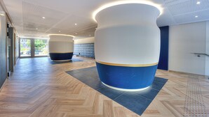 A modern interior with large cylindrical columns, a herringbone floor pattern, and a ceiling with recessed lighting. - Appartement Fleuri, vue mer - Welkeys (Saint-Laurent-du-Var)