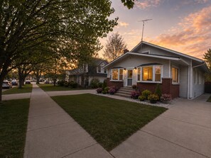 Uma casa suburbana com varanda da frente, entrada de automóveis e gramado bem cuidado.