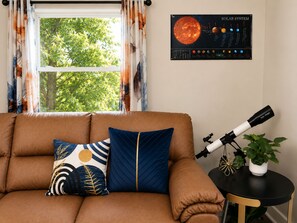 A room with a brown sofa, a poster of the solar system, a telescope, and a potted plant.