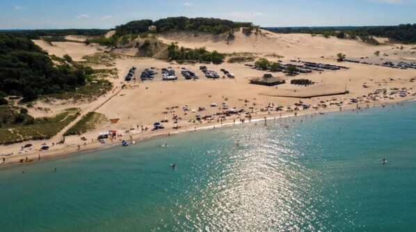 An aerial view of a beach with a parking lot and a sandy area with trees.