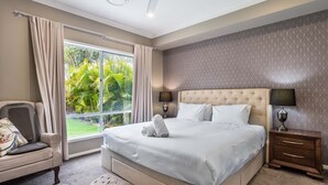 Habitación de hotel con una cama grande, dos mesitas de noche con lámparas, una silla y vistas a la vegetación por la ventana.