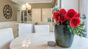 Un comedor con una mesa de mármol, un jarrón de rosas rojas y una cocina al fondo.