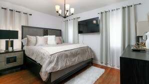 Un dormitorio con una cama, mesitas de noche, televisor y cortinas.