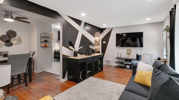 Una sala de estar moderna con un sofá negro, un comedor con una mesa blanca y una zona de cocina con un armario negro.