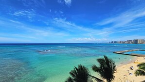 A beach with clear turquoise waters, a sandy shore, and a city skyline in the background.