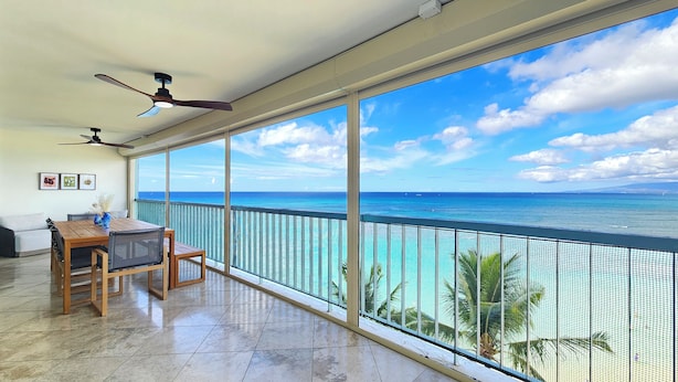 A balcony with a view of the ocean, a dining table with chairs, and ceiling fans.