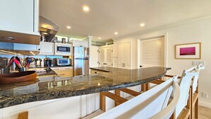 A modern kitchen with a curved granite countertop, stainless steel appliances, and white cabinetry.