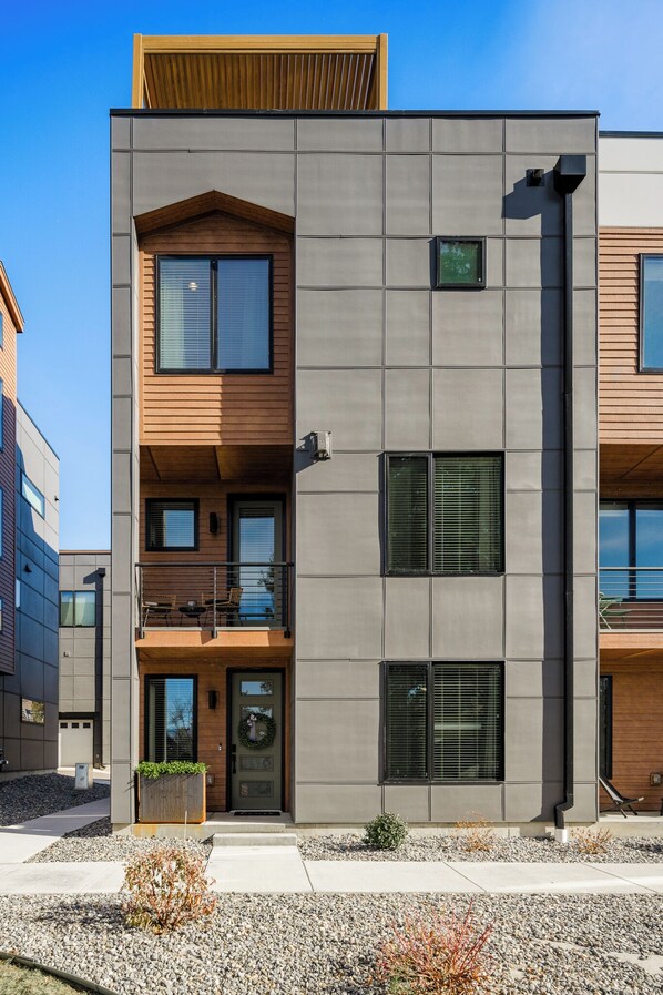 A modern multi-story building with a balcony, large windows, and a wooden door.