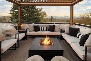 A rooftop patio with a fire pit, outdoor seating, and a view of the surrounding landscape.