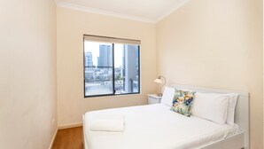 A hotel room with a large window, a bed with white linens, a nightstand with a lamp, and a tropical patterned pillow.