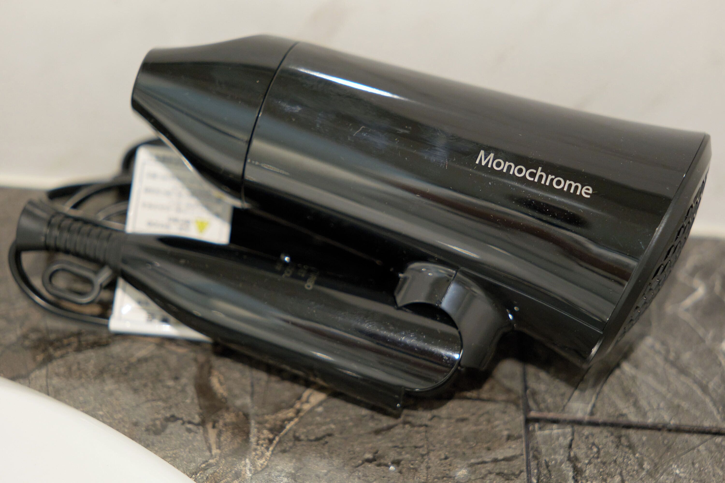 A black hair dryer with a cord and a tag on a tiled surface.