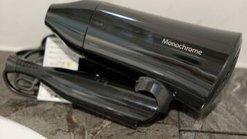 A black hair dryer with a cord and a tag on a tiled surface.