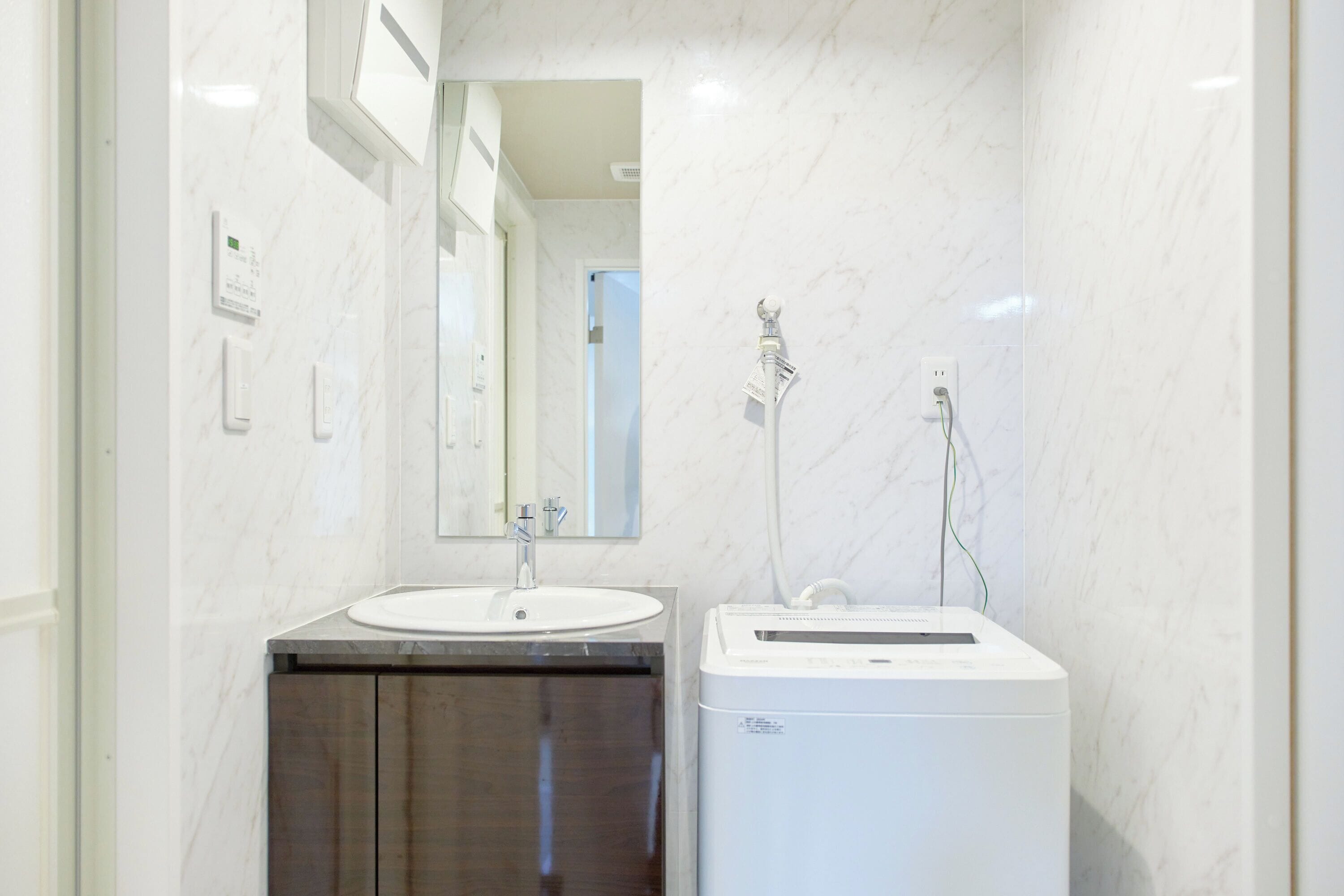 A bathroom with a marble wall, a sink, a mirror, and a white washing machine.