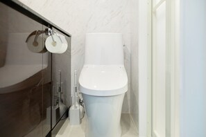A modern bathroom with a white toilet, a glass shower enclosure, and a marble wall. - The under suite residence Ikebukuro by Tranova (Tokyo)