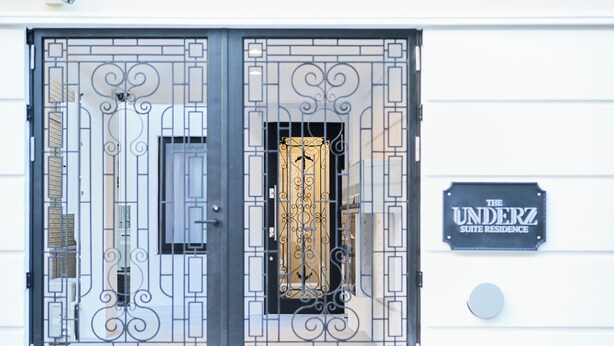 A double door with intricate metalwork, a sign reading "The Underz Suite Residence," and a round mailbox on the wall.