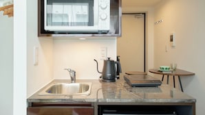 A compact kitchen with a built-in microwave, a sink, a coffee maker, and a small table with a cup.