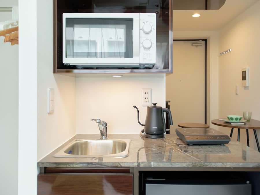 A compact kitchen with a built-in microwave, a sink, a coffee maker, and a small table with a cup.