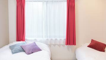 Una habitación con dos camas, una ventana con cortinas traslúcidas y un radiador.
