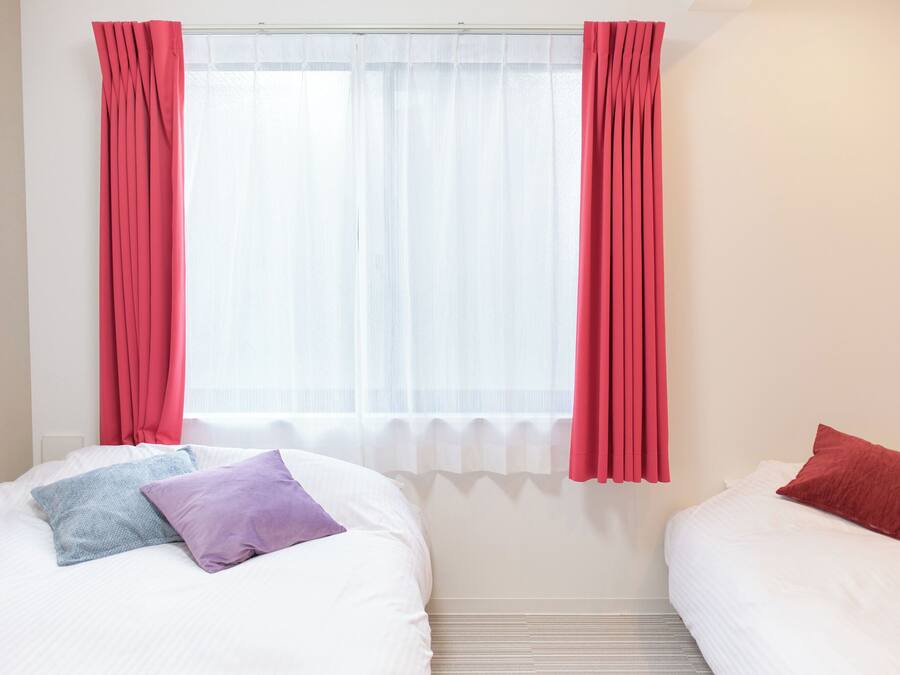 Una habitación con dos camas, una ventana con cortinas traslúcidas y un radiador.
