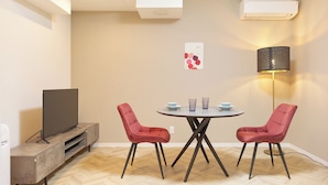 A modern living room with a flat-screen TV, two red chairs, a round table, and a floor lamp.