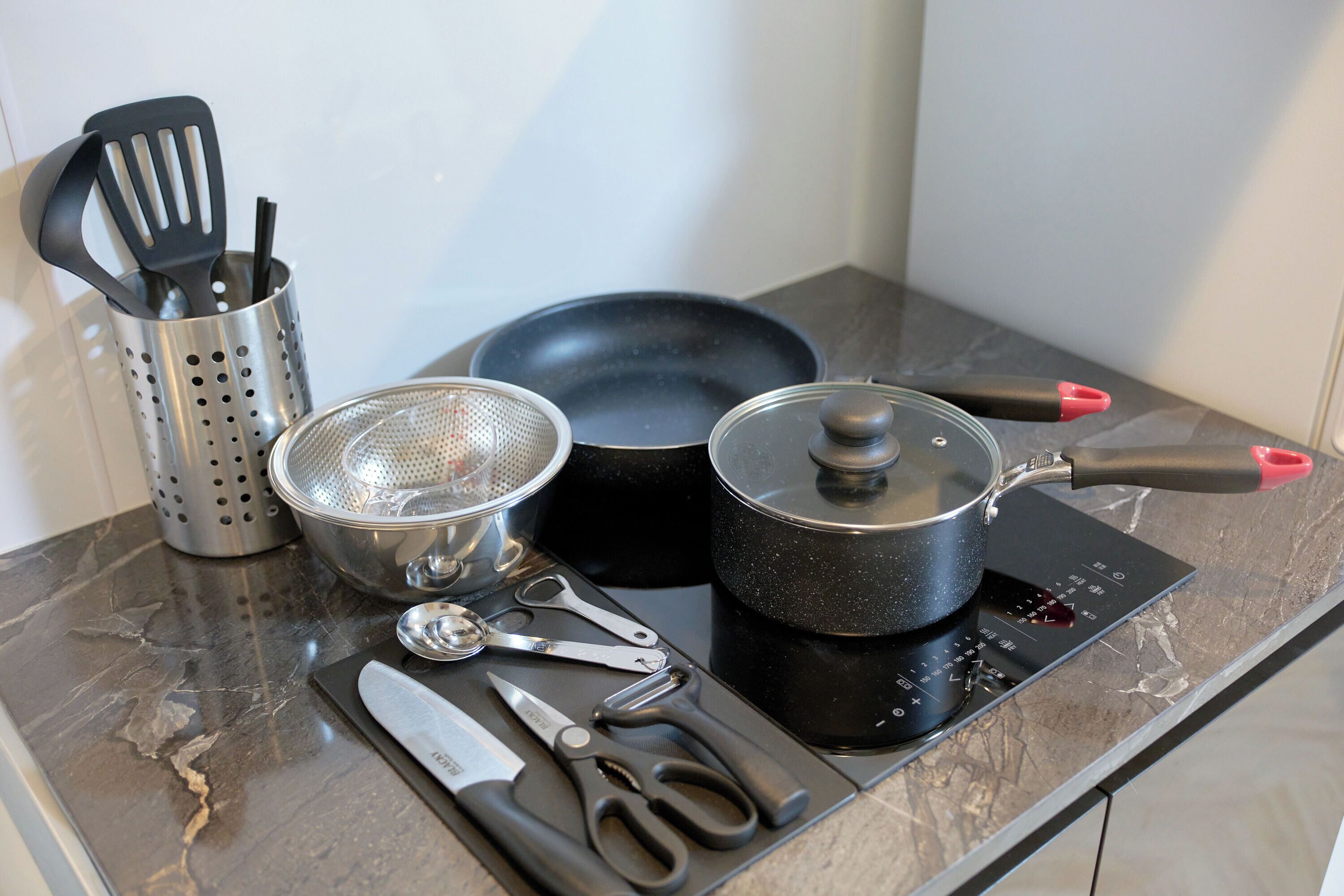 A kitchen counter with a frying pan, pot, strainer, spatula, and utensils.