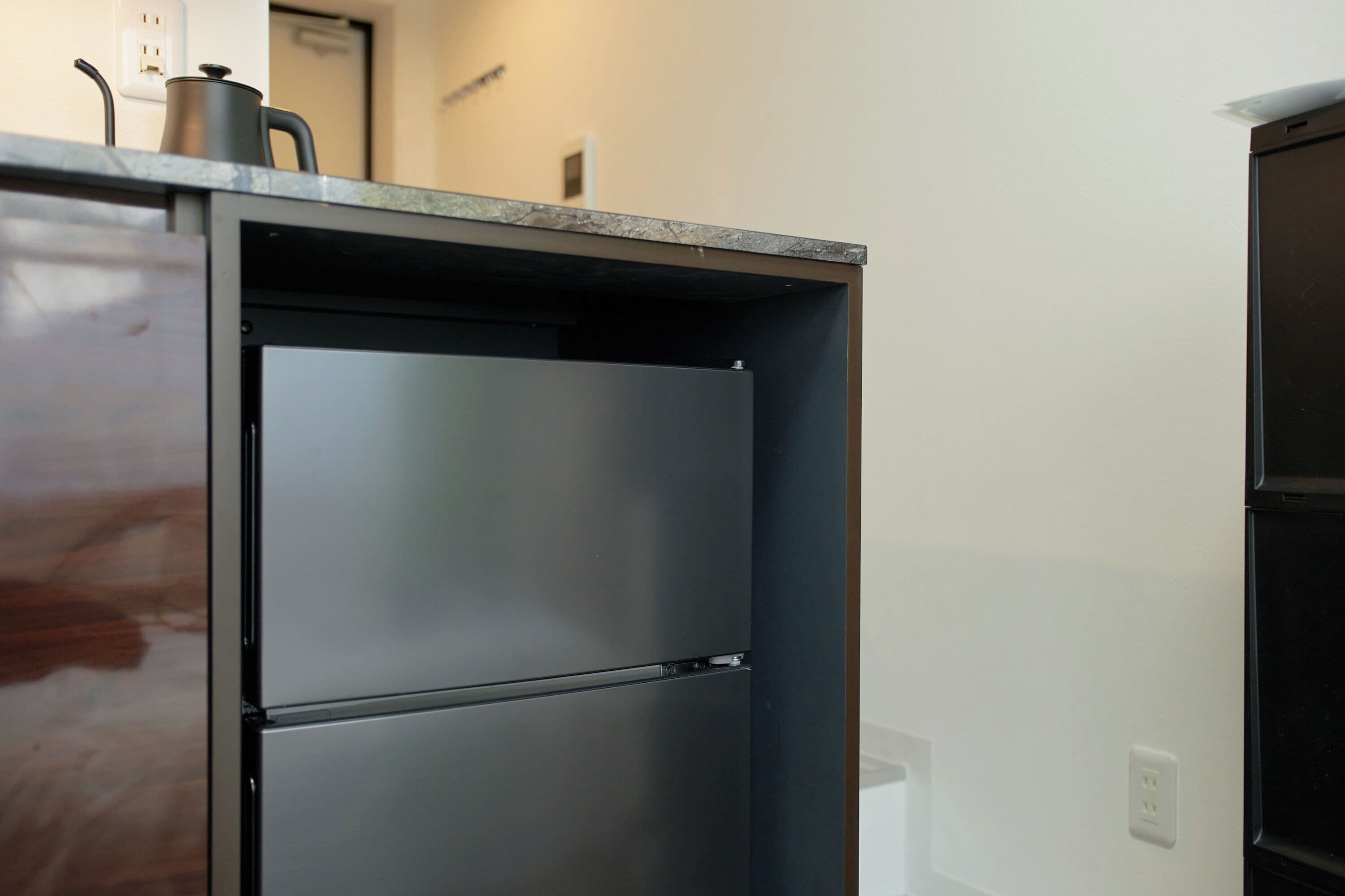 A kitchen with a built-in refrigerator and a kettle on the countertop.