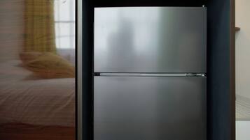 A modern, metallic refrigerator in a room with a wooden floor and a window with a curtain.