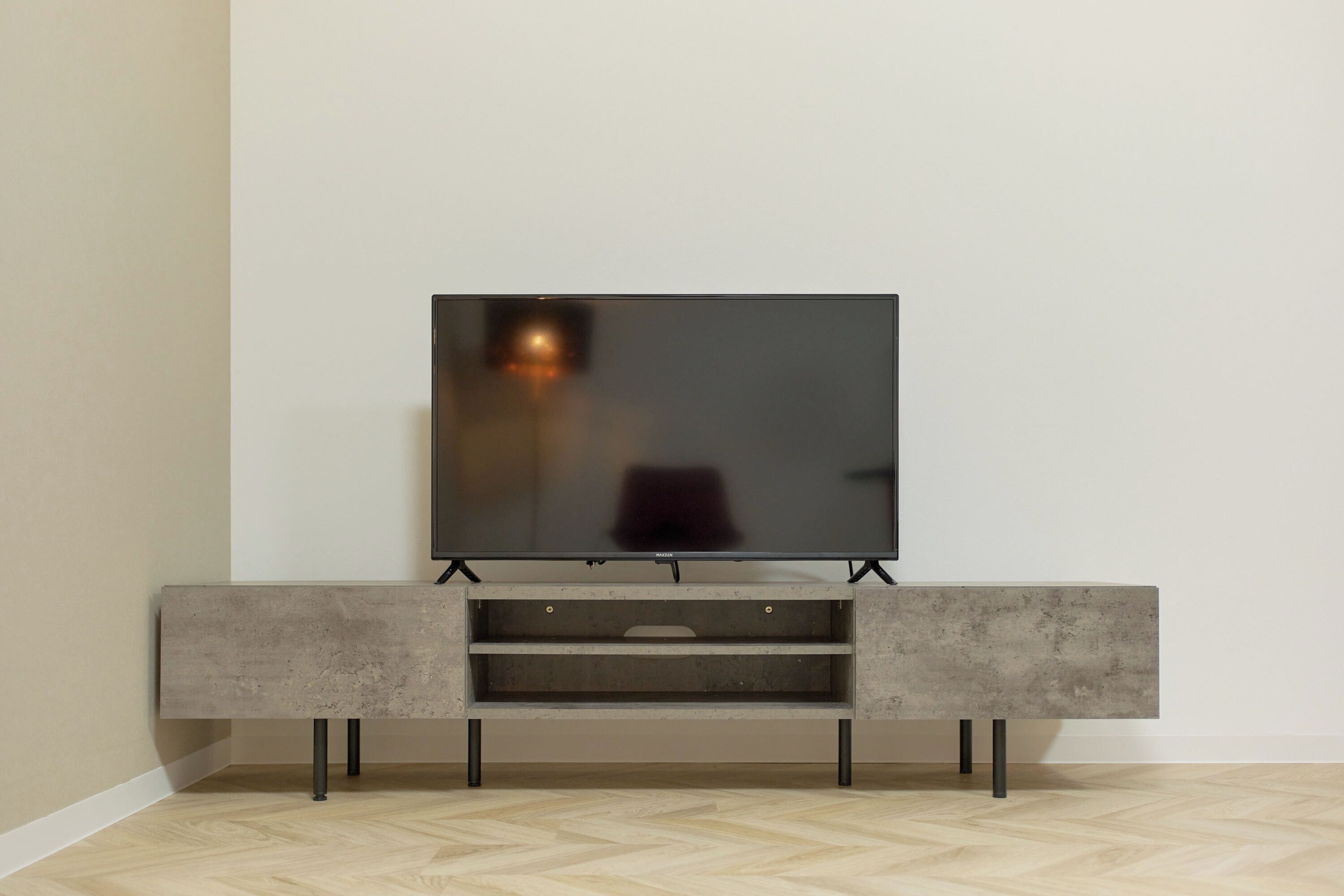 A flat-screen TV mounted on a minimalist entertainment unit with a herringbone-patterned wooden floor.