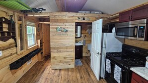 A rustic cabin-style kitchen with wooden walls, a ceiling fan, a microwave, a stove, and a sink.