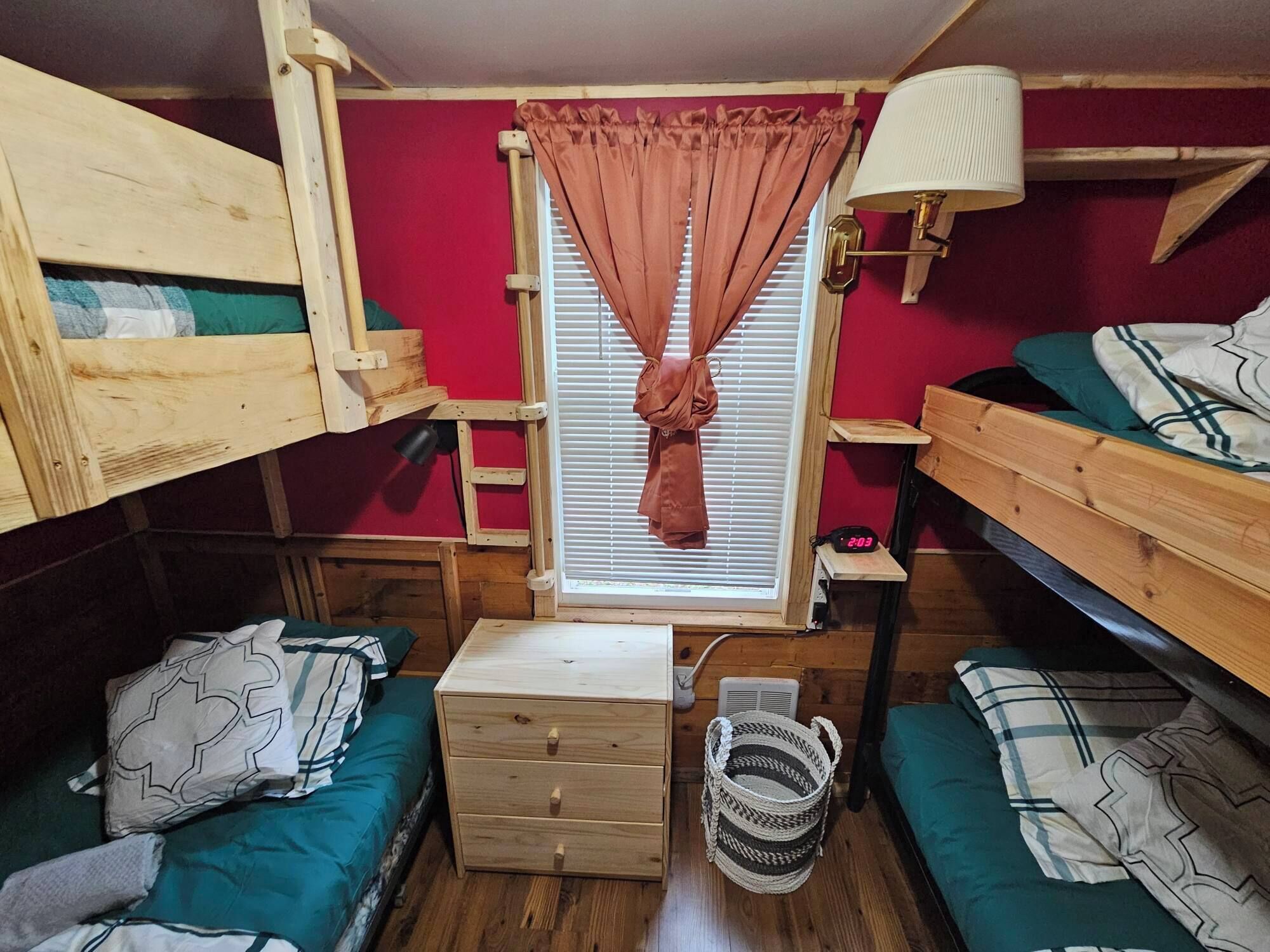 Et lille værelse med køjesenge, et lille bord, en lampe og et vindue med gardiner.