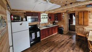 A rustic kitchen with wooden walls, a ceiling fan, a refrigerator, a stove, and a microwave.