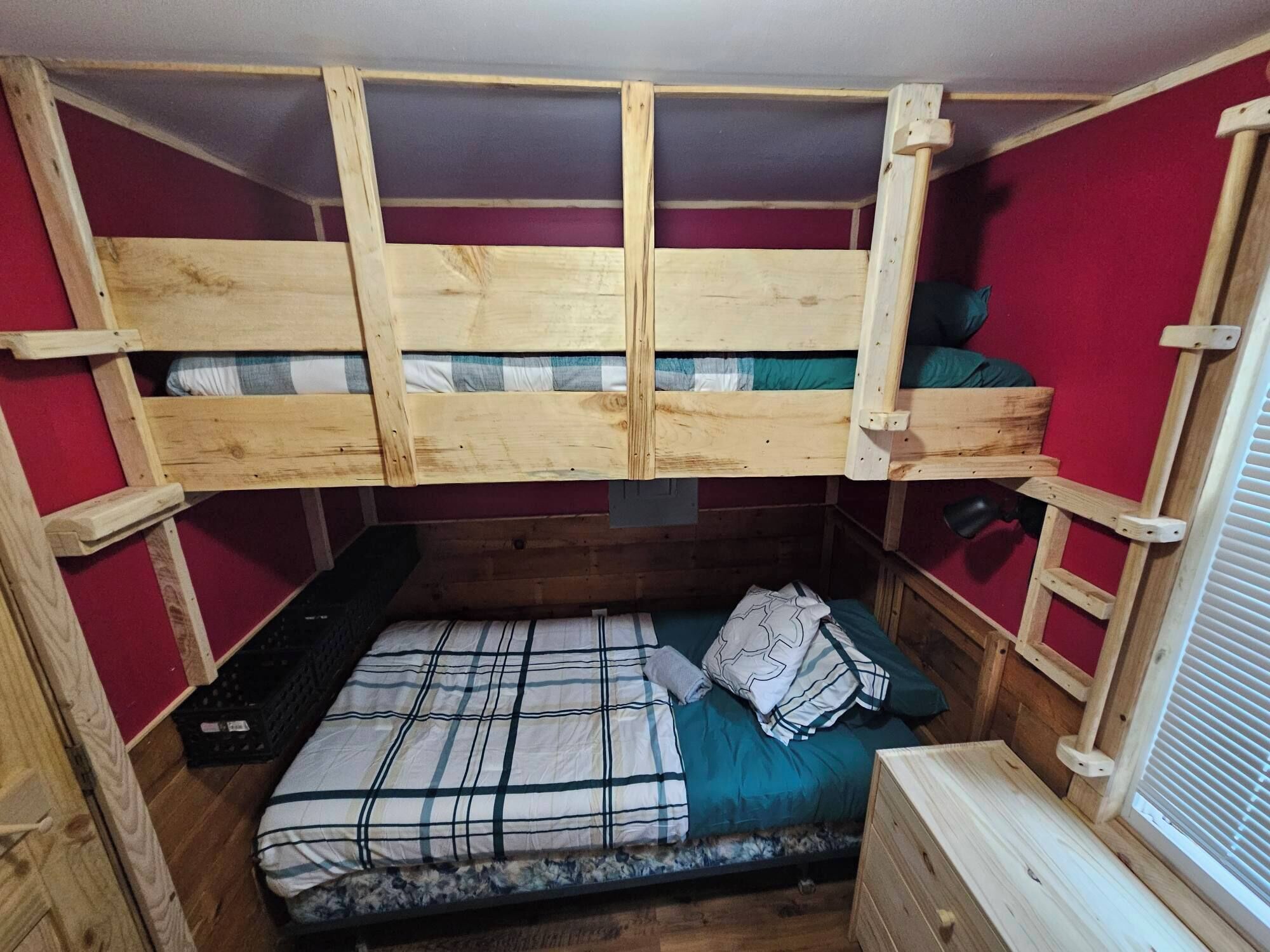 Habitación con literas compactas de madera, una cama individual con manta escocesa y una ventana con persianas.