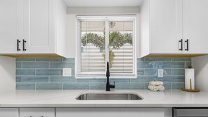 Una cocina con armarios blancos, un lavamanos de acero inoxidable y una ventana con persianas.