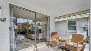 Une terrasse moderne avec des meubles en osier, une porte vitrée donnant sur un espace intérieur et une vue sur l’extérieur.